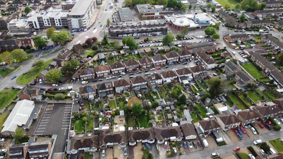 An aerial view of a residential area in Brockley, featuring a mix of terraced houses with small rear gardens and lawns, many with neatly trimmed hedges and flowerbeds. The gardens display a variety of